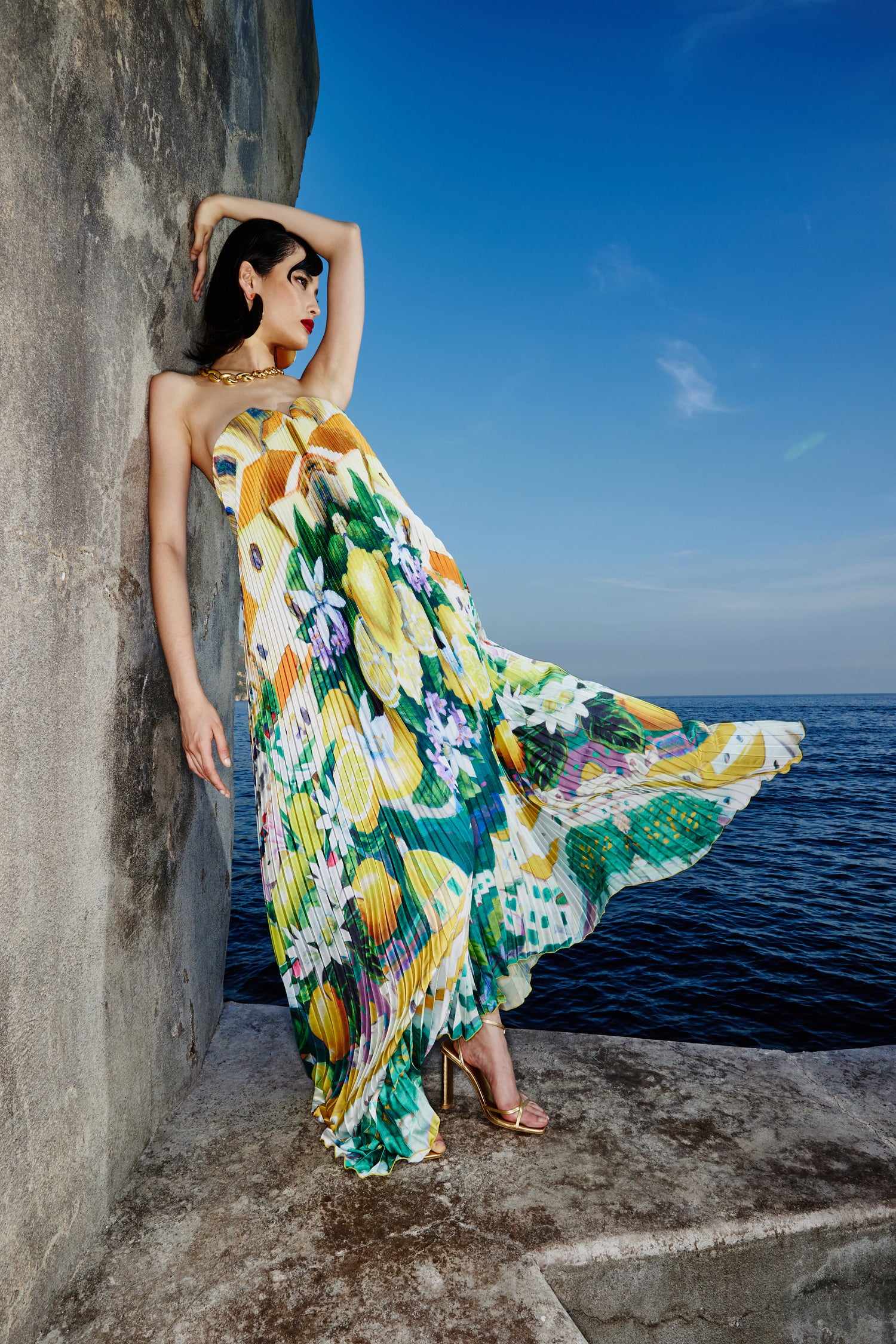 Woman in vibrant dress leaning against wall.