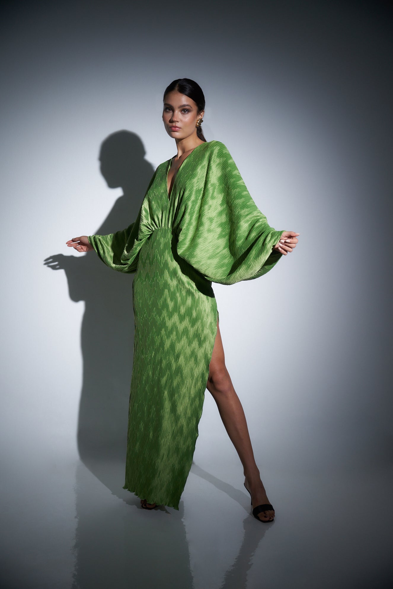 Model in a green long-sleeved dress with a high slit.