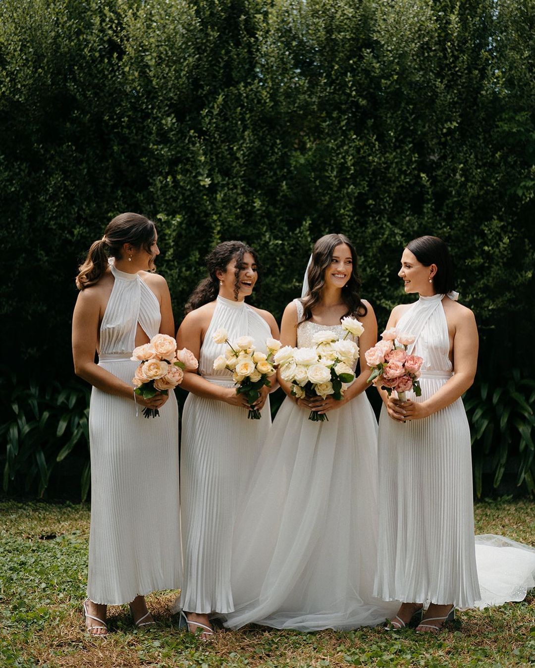 Bridesmaids in white dresses pose together in front of trees