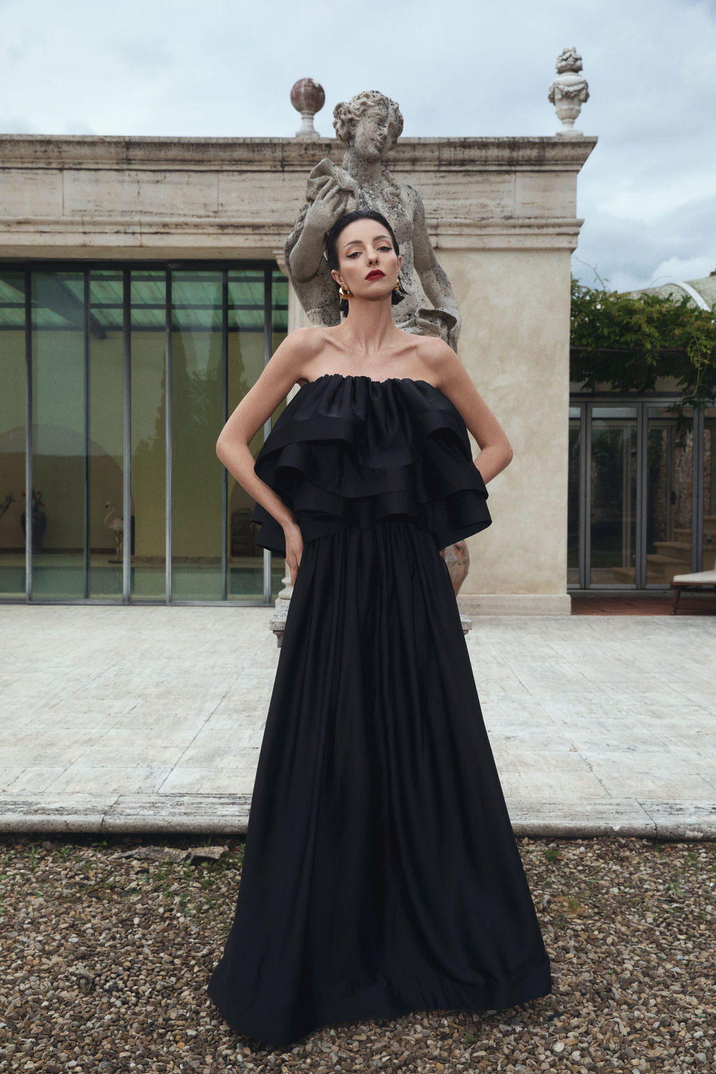 A woman in a black dress stands poised in front of a statue