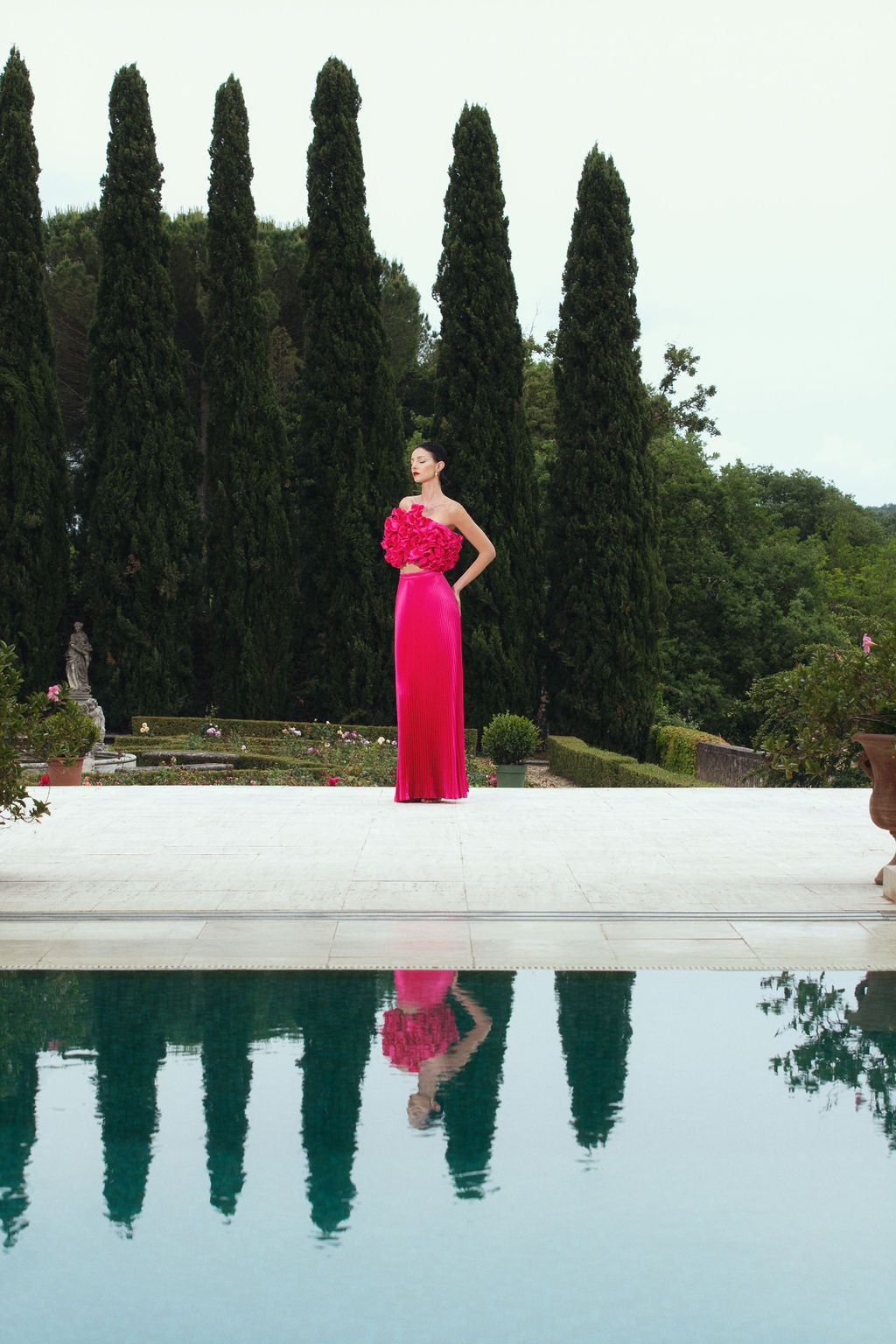 A woman in a pink dress stands near a calm pool