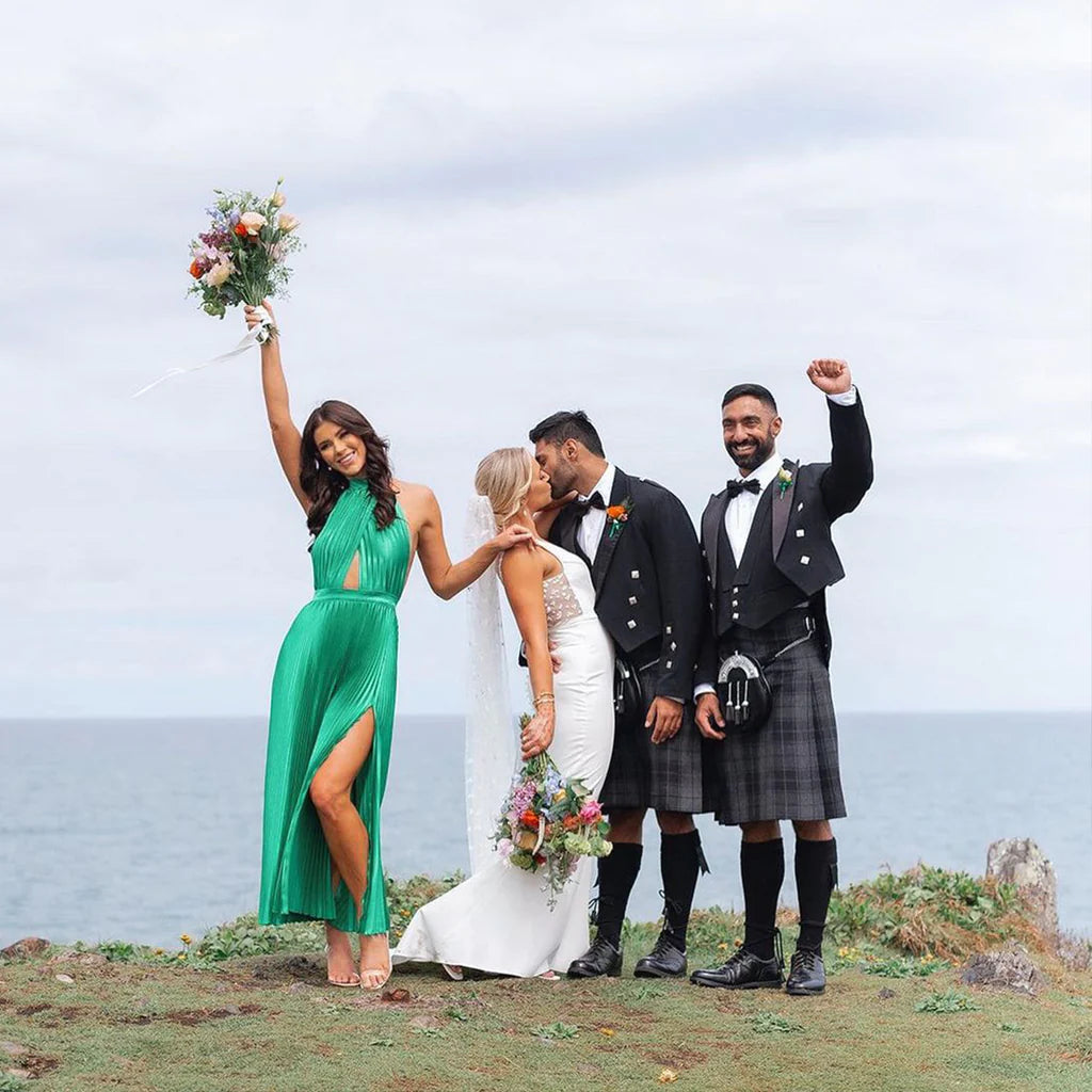 Bride and groom wearing kilts, surrounded by friends, posing happily for a group photo at a wedding.